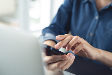 Closeup, woman using smartphone and laptop computer for online shopping, digital banking, social network via mobile app. Business woman using mobile phone and laptop working at office