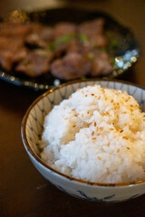 A bowl of rice served on the table, with Japanese Yakiniku meat on the background
