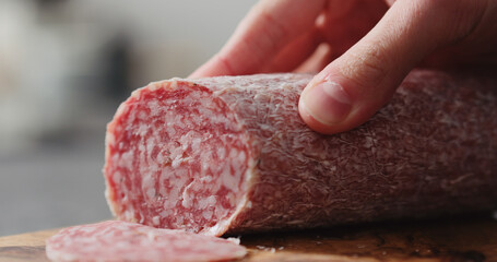 man slicing salame sausage on olive wood board