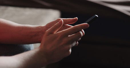 Closeup young man in black t-shirt typing messages on smartphone working from home side view