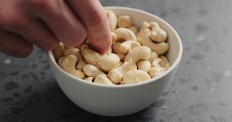 man hand takes cashew nuts from white bowl on terrazzo countertop