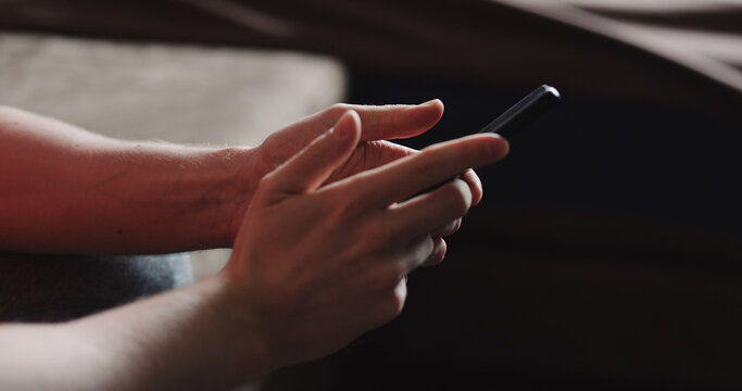 Closeup young man in black t-shirt typing messages on smartphone working from home side view