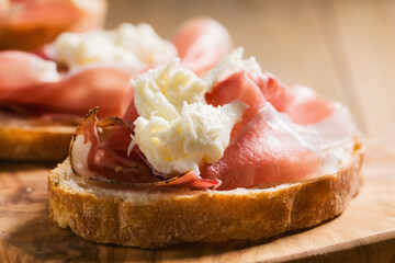 simple bruschetta with prosciutto and mozzarella on wood board