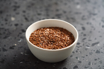 Flax seeds in white bowl on terrazzo surface with copy space