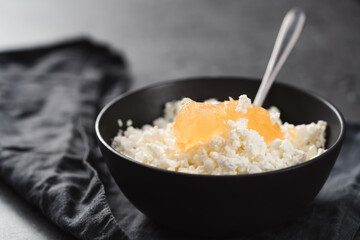 Cottage cheese with orange jam in white bowl on concrete background