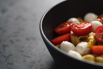 fettuccine pasta with pesto, mozzarella and cherry tomatoes in black bowl on concrete background closeup with copy space