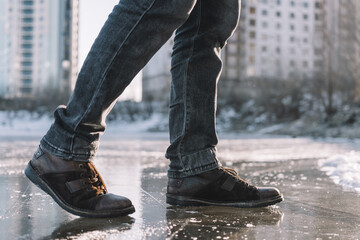 Boots standing on icy ground, illustrating the danger of slipping on a frozen, slippery winter surface. man walks cautiously along an icy street on a winter day for fear of slipping and falling.