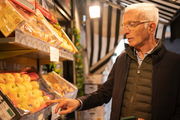 Senior man buying fresh apples on a fruit stall in a local outdoor market