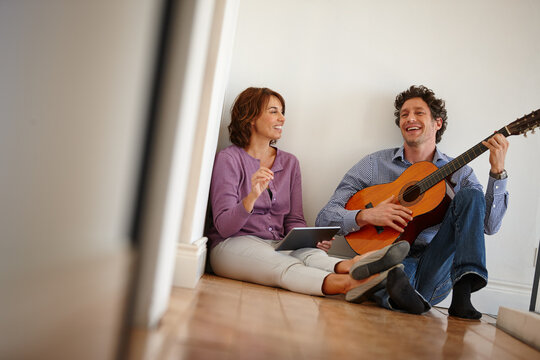 Love, guitar and couple on floor with tablet, lesson and bonding in home with music and creativity. Musician, man and woman with support, hobby and entertainment together in hallway with tech