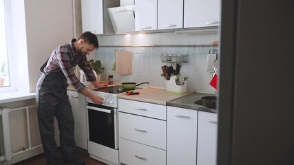 Caucasian man in overalls checks electric stove and removes heat controls for repair. Kitchen appliance maintenance and in-home repair. Service and DIY troubleshooting.