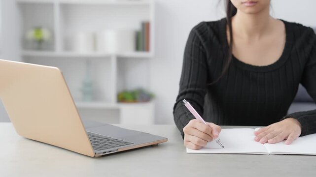 部屋でノートパソコンを見ながら勉強する女性