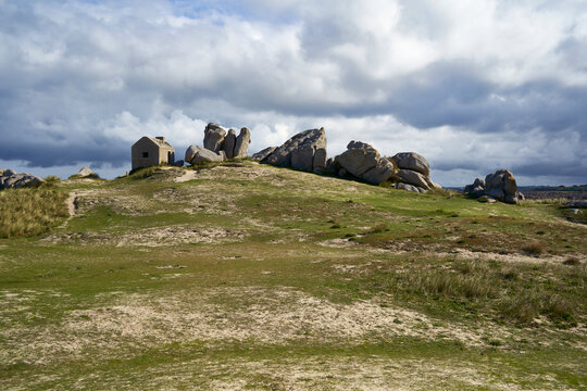 An old watchtower stands on a grassy hill, surrounded by large rocks under a cloudy sky, highlighting the historical charm of Brittany. Plage des Amiets, France.