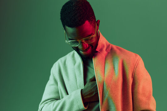 Stylish African American man in a light beige coat with glasses, smiling against a vibrant green background, exuding confidence and modern fashion trends - Powered by Adobe