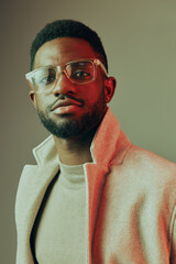 Portrait of a stylish Black man wearing glasses and a light coat, exuding confidence with a warm smile against a muted background, perfect for lifestyle and fashion themes