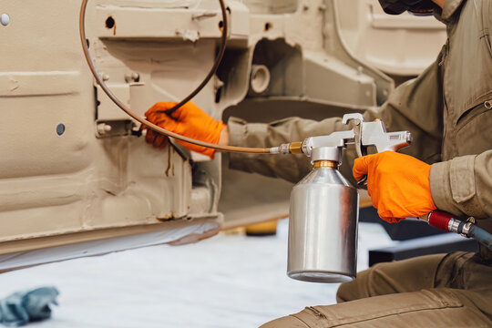 Specialist spraying anti rust sealant into the hidden chassis cavities. Protection against corrosion and internal body element sealing in a professional auto service shop