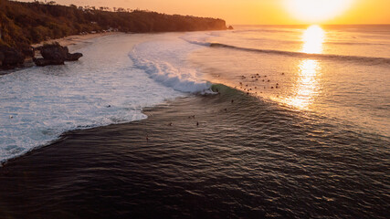 Surfers on Padang Padang on evening at sunset with perfect waves