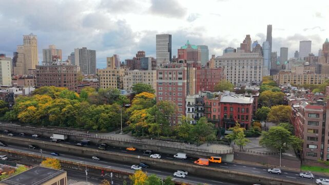 Cinematic aerial view of Brooklyn side New York City, New York showing skyline towers, leafy park trees and the busy FDR highway running along the waterfront creating a bright detailed urban scene