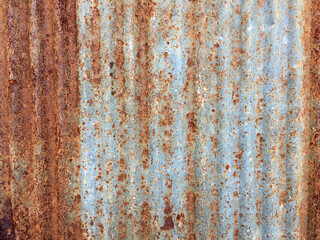 Full-frame view of heavily weathered and rusted corrugated metal sheeting, texture features distinct patches of vibrant orange, red, and deep brown rust against the faded, galvanized gray-blue surface