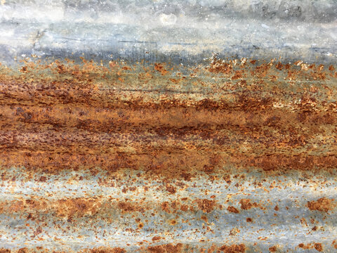 Full-frame view of heavily weathered and rusted corrugated metal sheeting, texture features distinct patches of vibrant orange, red, and deep brown rust against the faded, galvanized gray-blue surface