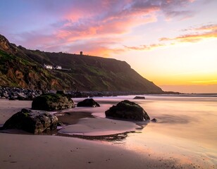 Sunset over beach with large rocks, cliffs, building, and vibrant sky