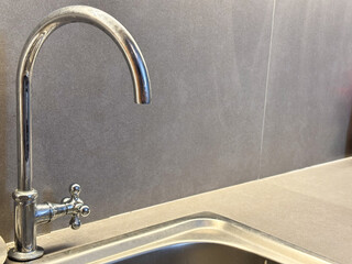 A close-up, vertical shot of a tall, gooseneck kitchen faucet made of shiny chrome or polished stainless steel.