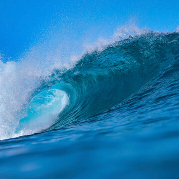 Massive blue ocean wave curling, bright turquoise barrel breaking with foamy crest and spray, sunlight