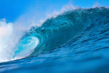 Massive blue ocean wave curling, bright turquoise barrel breaking with foamy crest and spray, sunlight