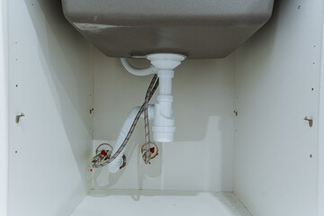 closeup of sink shutoff valves and braided hoses, metal connectors and supply lines visible against white cabinet back, practical detail shot for repair, parts, and installation
