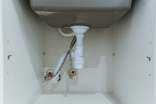 closeup of sink shutoff valves and braided hoses, metal connectors and supply lines visible against white cabinet back, practical detail shot for repair, parts, and installation