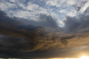 Fototapeta premium Dark swirling storm clouds illuminated by low golden light with layered textures