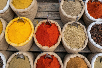 Overhead view of colorful spices and herbs in burlap sacks with metal scoops at a market.