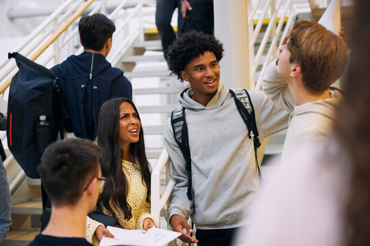 Confused teenage girl standing with male friends in high school corridor