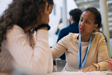Female professor consoling teenage student while sitting in high school lobby