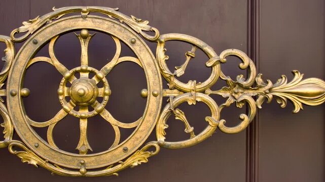 Decorative, ornate, golden-toned metalwork, possibly part of a gate, set against a dark wooden background