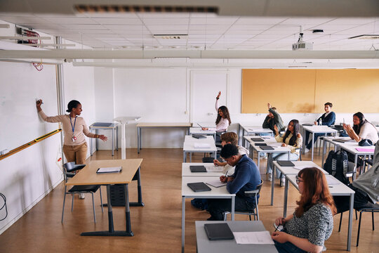 High angle view of female teacher asking questions to students while teaching in classroom at school