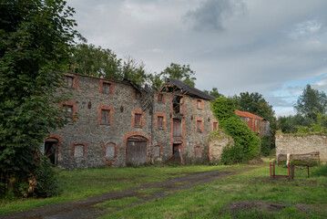 Ruins of an abandoned, industrial building shows crumbling stone and brick, with boarded-up windows and ivy climbing the surface. Photo taken in Inniskeen, County Monaghan, Ireland