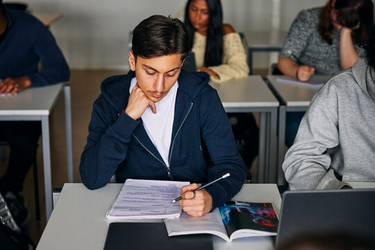 Concentrated teenage male student studying while sitting at desk in high school classroom