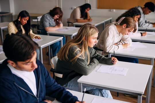 High angle view of male and female students giving exam while sitting at desk in classroom