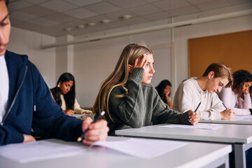 Stressed female teenage girl looking away while sitting at desk in high school classroom