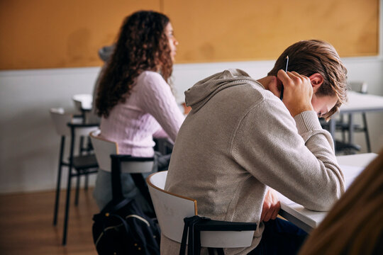 Tensed young male student sitting for educational exam with face down in classroom