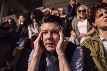 Stressed mature man touching temples while sitting in sports stadium