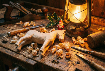 Hand carved wooden horse toy on carpenter workbench with chisel tools shavings and lantern in Christmas atmosphere