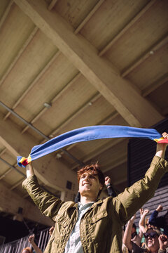 Low angle view of excited young man cheering while holding sports scarf in stadium stand
