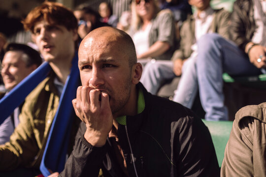 Concentrated bald man biting nails while watching game from stadium stand