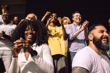 Low angle view of happy male and female supporters enjoying in stadium stand on sunny day