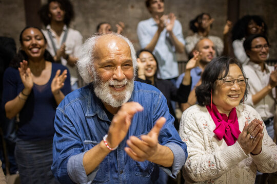 Smiling senior male and female spectators clapping while enjoying stage play in theater