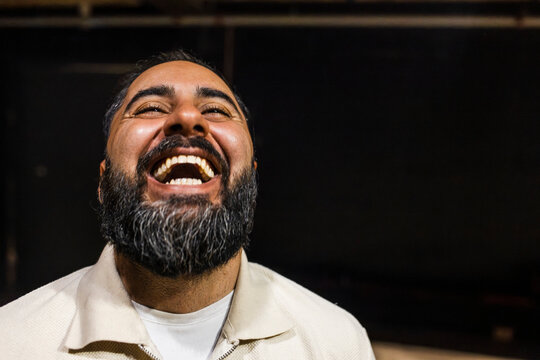 Headshot of carefree bearded man laughing in stage theater