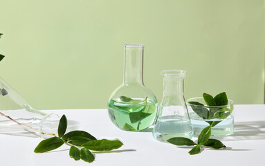 Green tea leaves and clear laboratory vessels sit on a light-colored table, forming a gentle and natural composition for cosmetic ingredient photography. Advertising photo