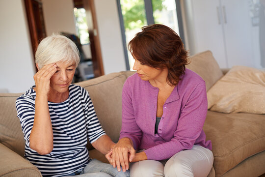 Headache, holding hands or senior mother with daughter on sofa, hypertension symptoms or family comfort. Retirement health problem, support or women in home to help, vertigo or migraine for brain fog