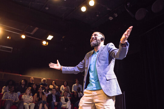 Low angle view of smiling male presenter wearing headset with arms outstretched talking in seminar at illuminated theate